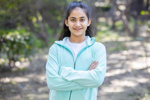 Portrait of beautiful young indian teenager girl stand cross arms while standing in the park outdoor, Smiling asian female child looking in the camera with attitude of success.