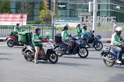 Thai express delivery motorcycle drivers are crossing a junction on Phahonyothin Road between Phaha Thai and Chatuchak. People are driving for different brands and companies.
