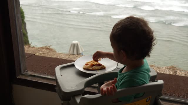 baby eating pizza with beach at the view