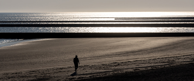 a man walking on a beach in the lower evening sun panorama