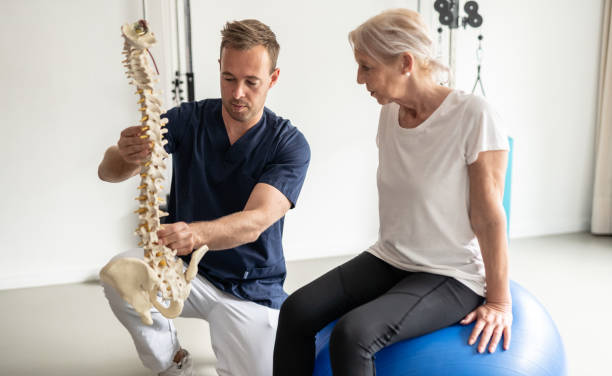 médico profesional que muestra al paciente anciano a través de ejercicios terapéuticos en un balón medicinal. - backache chiropractic adjustment pain women fotografías e imágenes de stock