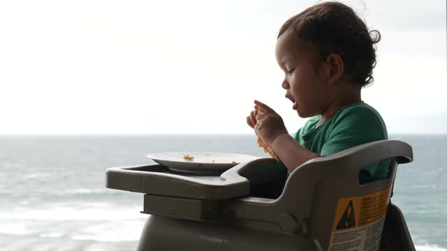 baby eating pizza with beach at the view
