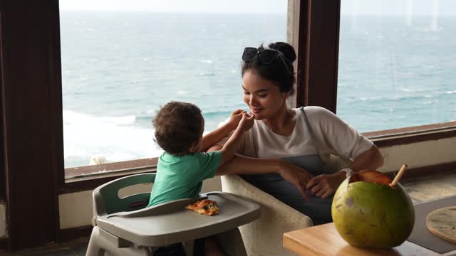 asian woman with her son sitting on the chair eating pizza