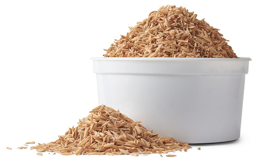 cup of paddy husk or rice husk, aka yellow rice chaff, rice husk or rice hull, outermost layer of the rice grain to use as animal feed, scattered isolated on white background, side view