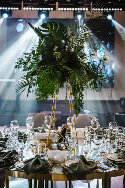 istock Banquet decoration composition flower greenery in hall. Luxury wedding reception. Table setting, setup. Trendy decor for birthday party. Round served tables for guests, plate, glasses, green napkins. 1525359289