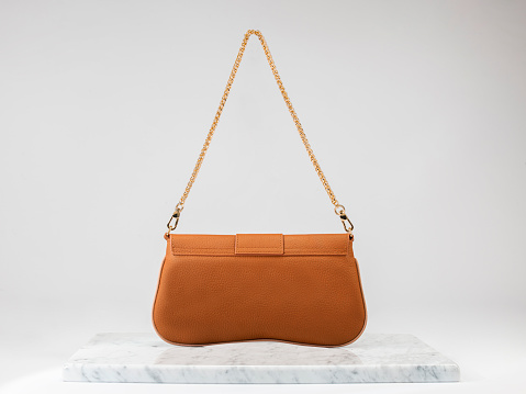 Luxury women 's bag. Luxury orange leather handbag on white background, on marble floor. A bag with a gold chain. Fashionable accessories for women. back side