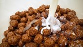 super close up. milk is poured into breakfast cereals chocolate corn balls. Milk pouring into bowl with chocolate balls. Chocolate flakes are poured with milk.