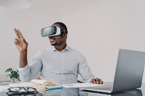 Black businessman: VR glasses, cyberspace work on laptop. Manager uses high-tech gadget, augmented reality, business.