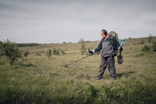 Man in sportswear with a metal detector. Digger on a summer meadow. The concept of searching for coins underground. Digger with metal detector.