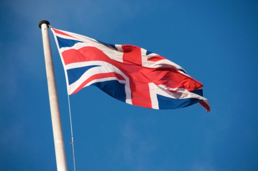 Landscape photo of a Union Jack Flag flying against a blue sky on a windy day