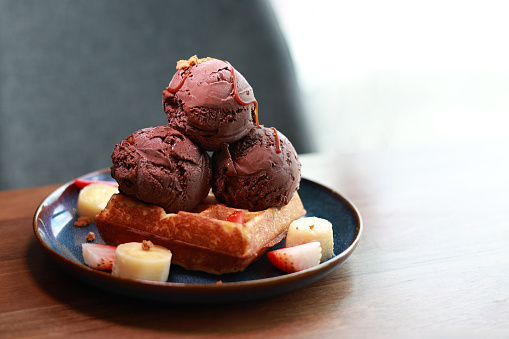 A mouth-watering Belgian waffle dessert topped with chocolate ice cream, fresh strawberries and banana slices, and a decadent chocolate drizzle