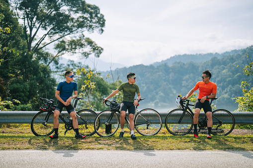 3 Asian chinese men road bike cyclist side by side at rural scene in the morning resting talking