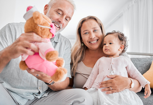 Mature, couple and baby with a toy while babysitting grand daughter with love, care and affection for fun playing. Caring, living room and grandfather, grandmother and child bonding with teddybear