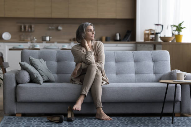 istock Tired serious middle aged grey haired woman sitting on couch 1525380878