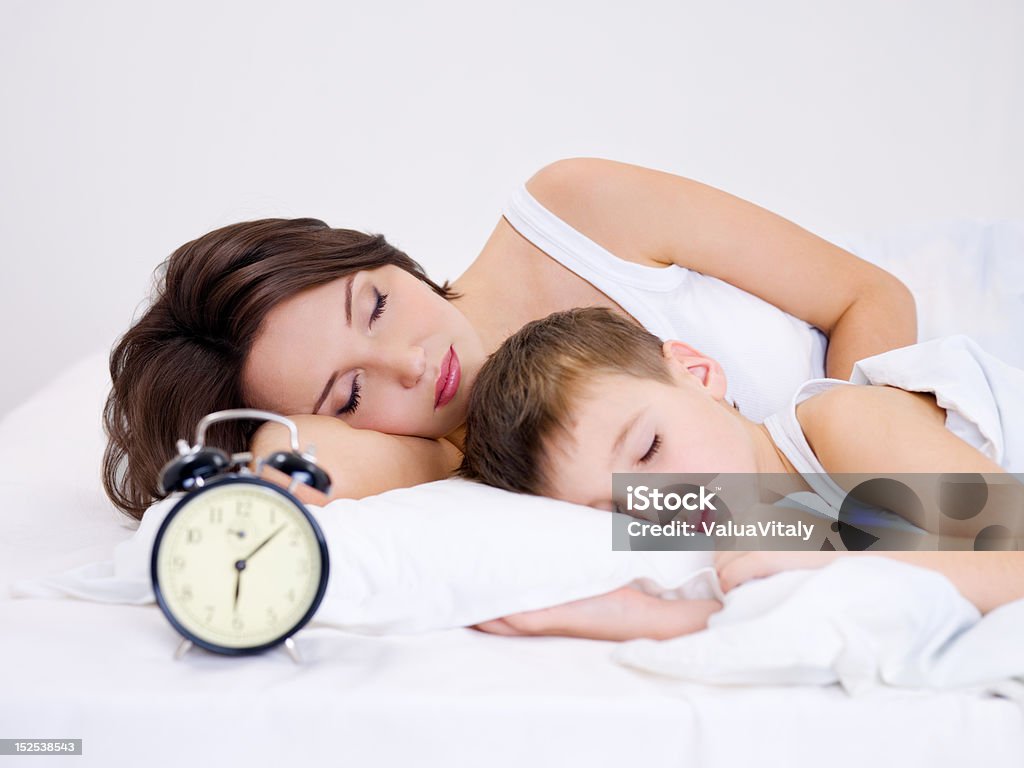 mother and son sleeping Young mother and son sleeping on a bed. &#192;larm clock on foreground Adult Stock Photo