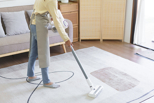 Maid using cordless vacuum cleaner to vacuuming and cleaning the dust on the carpet in home.