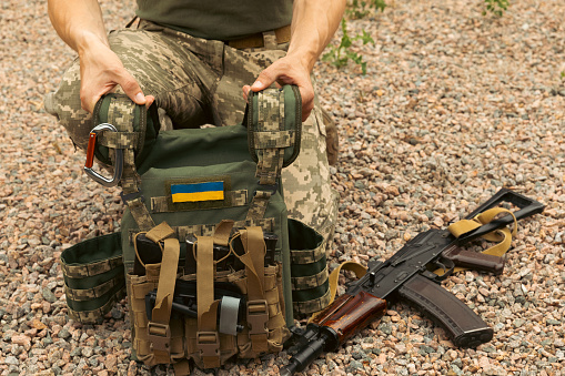 A soldier in a camouflage tactical uniform and a military body armor on a background of wood and greenery. Body armor with combat butts. Ukrainian army. Military concept. No war.medical tourniquet.