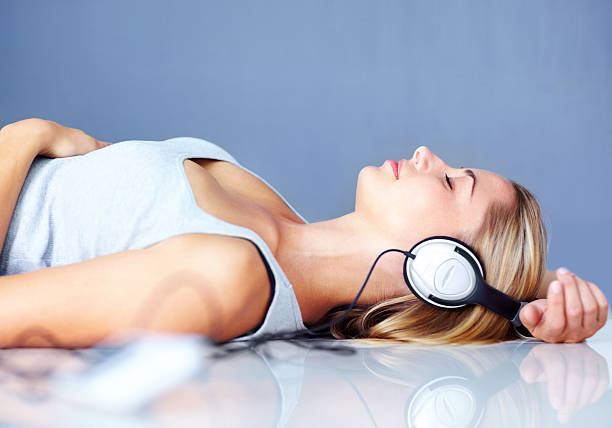 Young lady lying on floor while listening to music Side view of a young lady lying on floor while listening to music on headphones woman lying on the floor isolated stock pictures, royalty-free photos & images