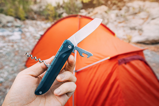 multitool foldable knife against camping tent background during hike