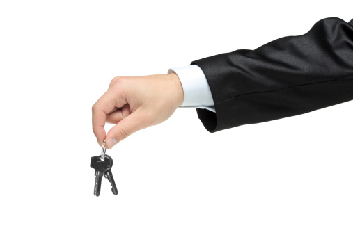 Man in a black suit holding keys isolated on white background