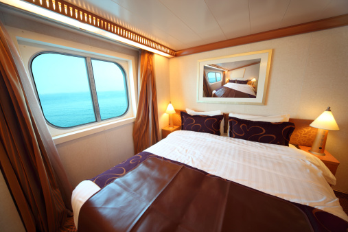 Ship cabin with big double bed and window with view on sea summer day