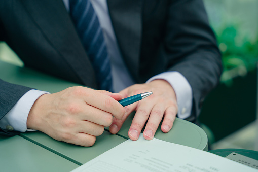 It’s a close up shot of a male financial planner’s hand who is holding a green pen.