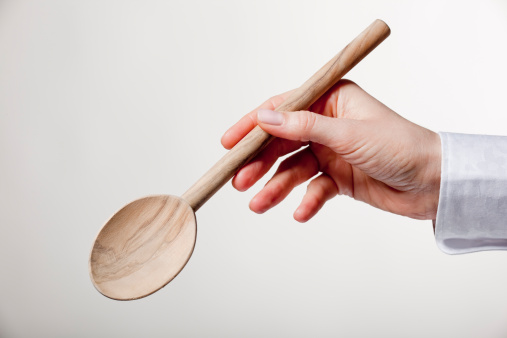 Female hand holding wooden spoon isolated on light background