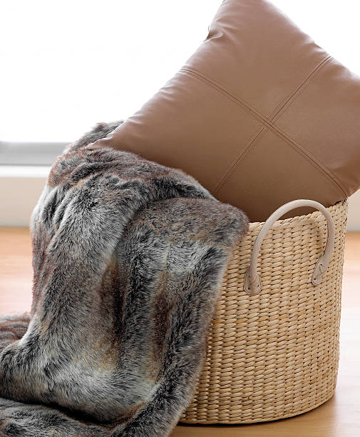 フェイクファーのラグにブラウンのクッション付きの籐のバスケット - homewares cushion fake fur blanket ストックフォトと画像