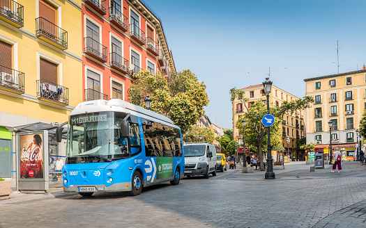 Madrid, Spain - June 27, 2023: New electric bus running by narrow cobblestone streets at the popular Plaza de Lavapiés, of Madrid. Lavapiés is a historic neighborhood in the city of Madrid, Spain. Lavapiés was considered for a long time the most \