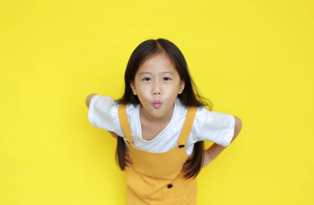 engraçado criança asiática expressão boca para fazer um beijo sobre fundo amarelo. criança com gesto de amor e olhando câmera - smiling humor child making a face - fotografias e filmes do acervo