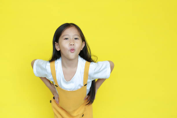 adorável menina asiática expressão boca para fazer um beijo no fundo amarelo. criança com gesto de amor e olhando câmera - child making a face human face humor - fotografias e filmes do acervo