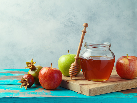 Honey jar, red apples and pomegranate on wooden blue table. Background for Jewish holiday Rosh Hashanah