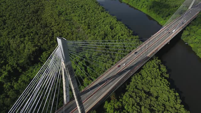 Aerial flight along of large suspension bridge over the river with cars traffic at sunrise. The Mauricio Baez cable-stayed Bridge. San Pedro de Macoris, Dominican Republic