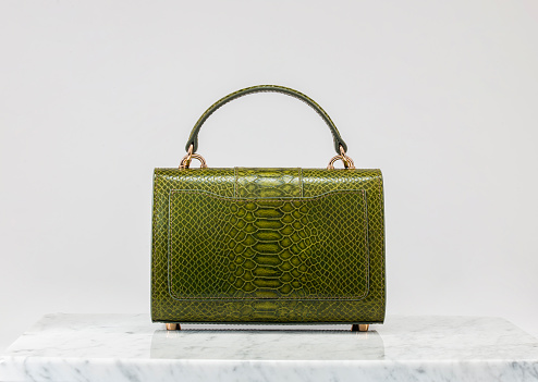 Luxury women 's bag. Luxury green leather handbag on white background, on marble floor. Crocodile skin look in green tones