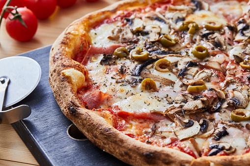 Pizza Capricciosa on a rustic cutting board, \nserved on a kitchen or restaurant table, with fresh vegetables, herbs and spices, representing a wellbeing and indulgence in food, city life and modern culture lifestyle