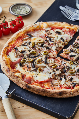 Pizza Capricciosa on a rustic cutting board, 
served on a kitchen or restaurant table, with fresh vegetables, herbs and spices, representing a wellbeing and indulgence in food, city life and modern culture lifestyle