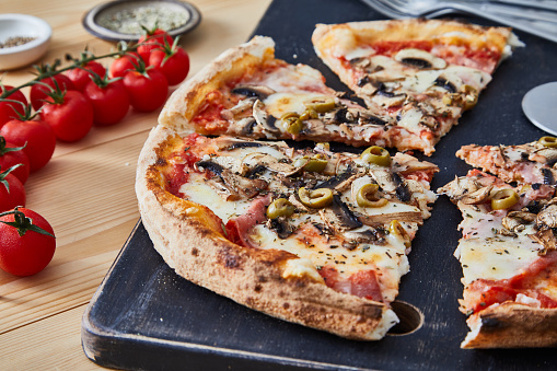 Pizza Capricciosa on a rustic cutting board, 
served on a kitchen or restaurant table, with fresh vegetables, herbs and spices, representing a wellbeing and indulgence in food, city life and modern culture lifestyle