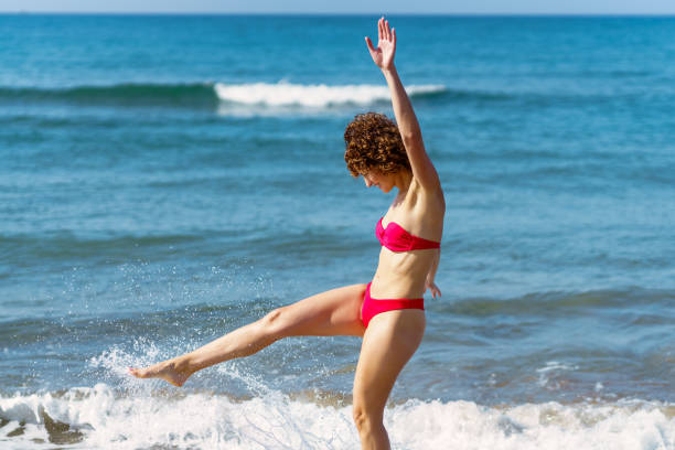 istock Delighted young lady kicking waves on beach on sunny day 1525679297
