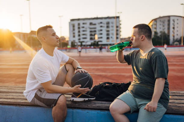 istock A man with Down syndrome drinks water from a plastic bottle while sitting on a basketball court with his friend 1525821842