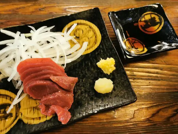 Horsetail meat raw sashimi with wasabi, ginger, soy sauce on wooden table by top view in Japanese restaurant. Food industry.