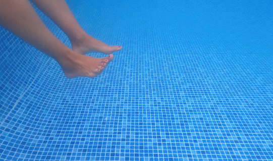Underwater image of legs in a blue tiled pool with copy space. Summer funny image