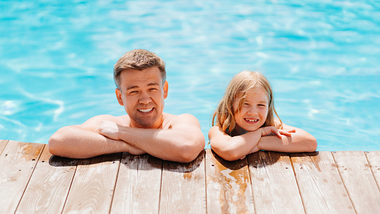 Dad and daughter have fun and and pose at the edge of the pool. family holidays and sports with children. Happy family. Father's Day.