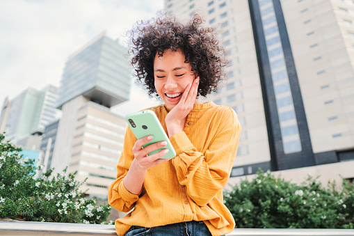 One young adult woman using a cellphone surprised by good sales. Female watching shocked the screen of the smart phone. Successful, excited, glad, happy and amazed girl with victory face expression. High quality photo