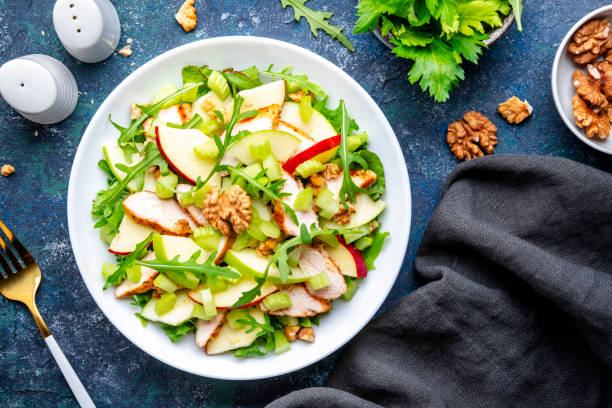 istock Waldorf salad with fresh apple, celery, lettuce, grilled chicken fillet, arugula and walnuts on plate, blue table background, top view 1525961716
