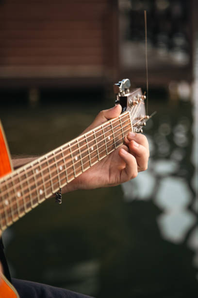 mężczyzna gra na gitarze, siedząc na drewnianym molo w pobliżu jeziora. - playing an instrument vertical blurred motion outdoors zdjęcia i obrazy z banku zdjęć