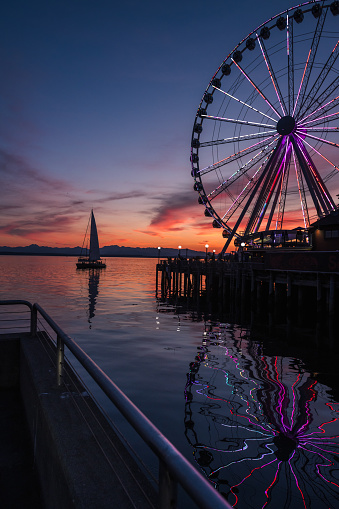 Seattle, USA - Jun 27, 2023: Sunset over Elliott Bay on the waterfront with a Sailboat and the Seattle Great Wheel.