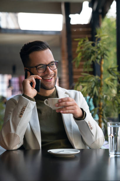 istock Handsome smiling businessman in suit talking on cell phone while drinking coffee in Cafe 1526199767