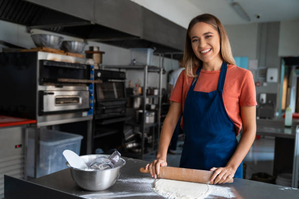 istock Beautiful woman rolling dough on table with flour in bakery 1526204451