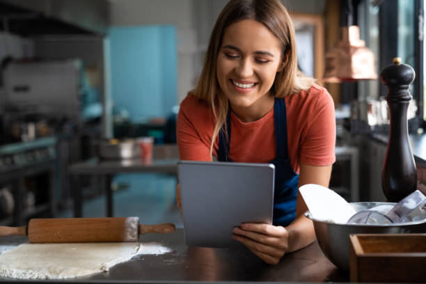 istock Beautiful happy female baker looking at digital tablet while working in the bakery 1526205506