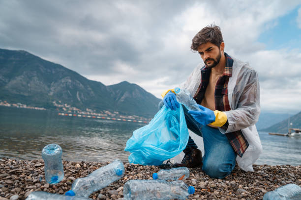 istock Unhappy sorrowful young man looking at the plastic bottle while kneeling and picking them up from the rocky beach 1526216827